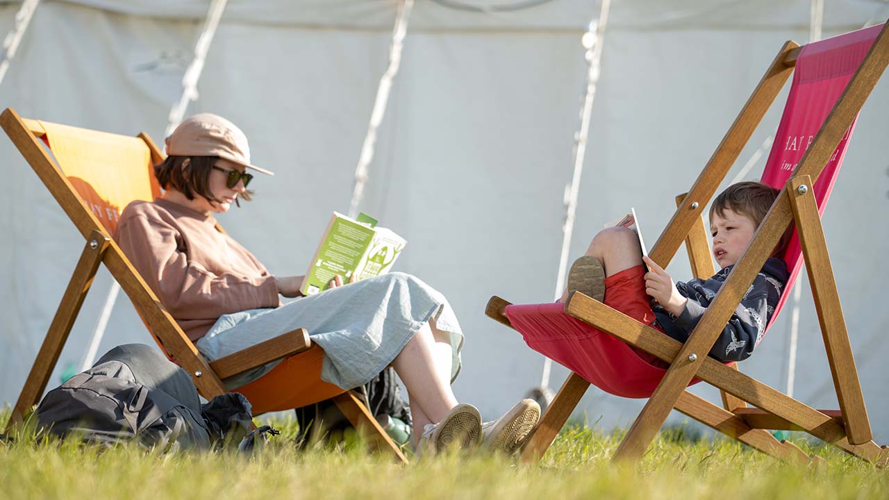 Parent and child sat on deck chairs and reading books at Hay Festival