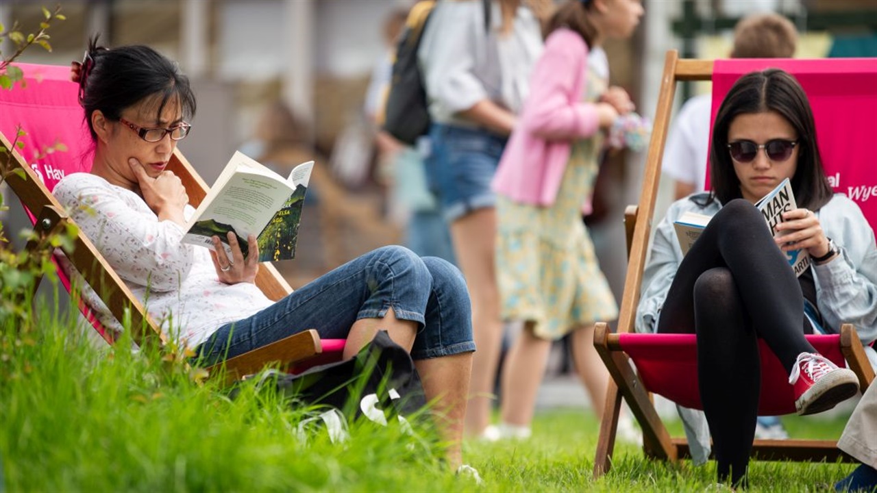 Two readers sitting on deck chairs outside at Hay Festival 2024